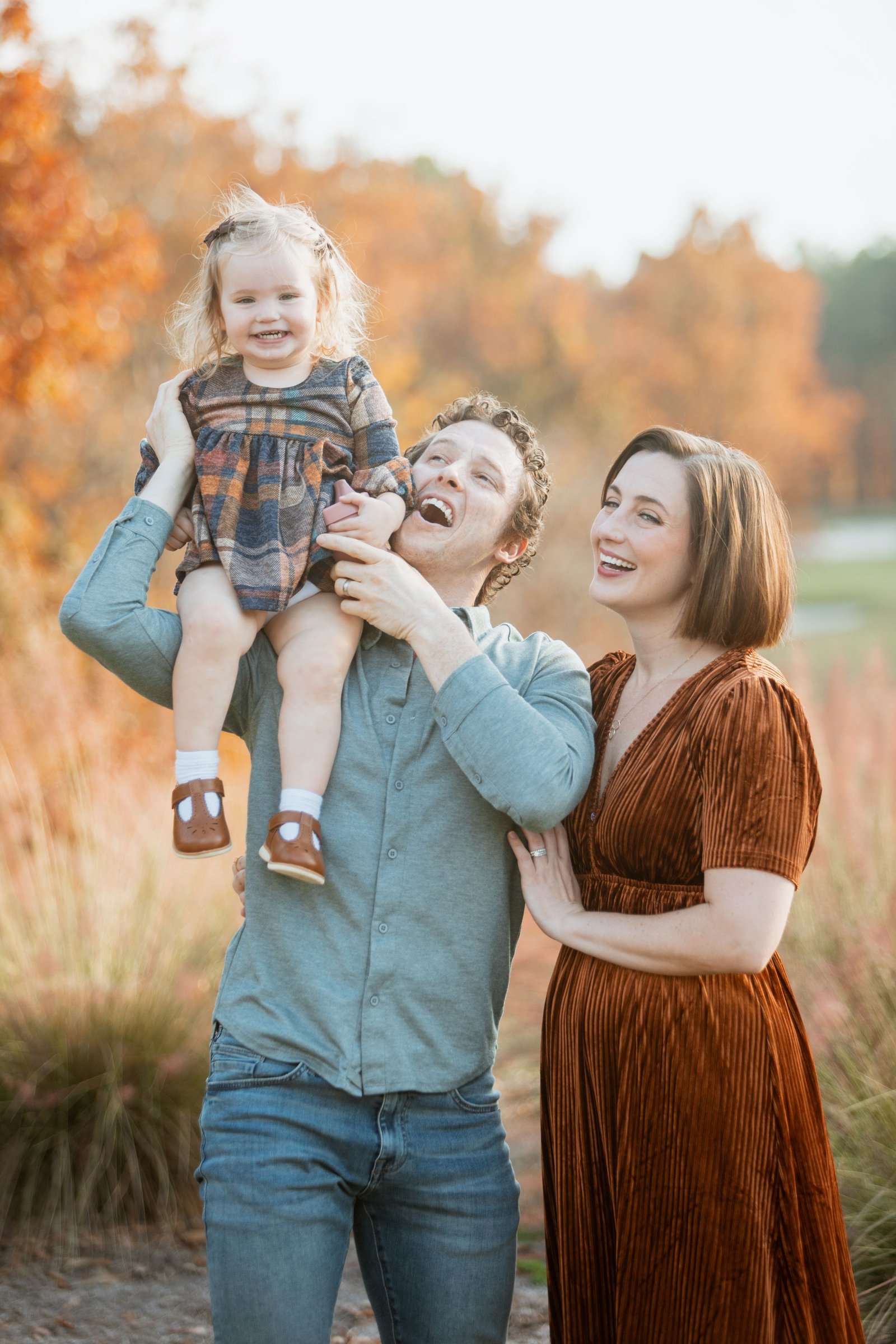 Parents lift their toddler during an autumn family session.