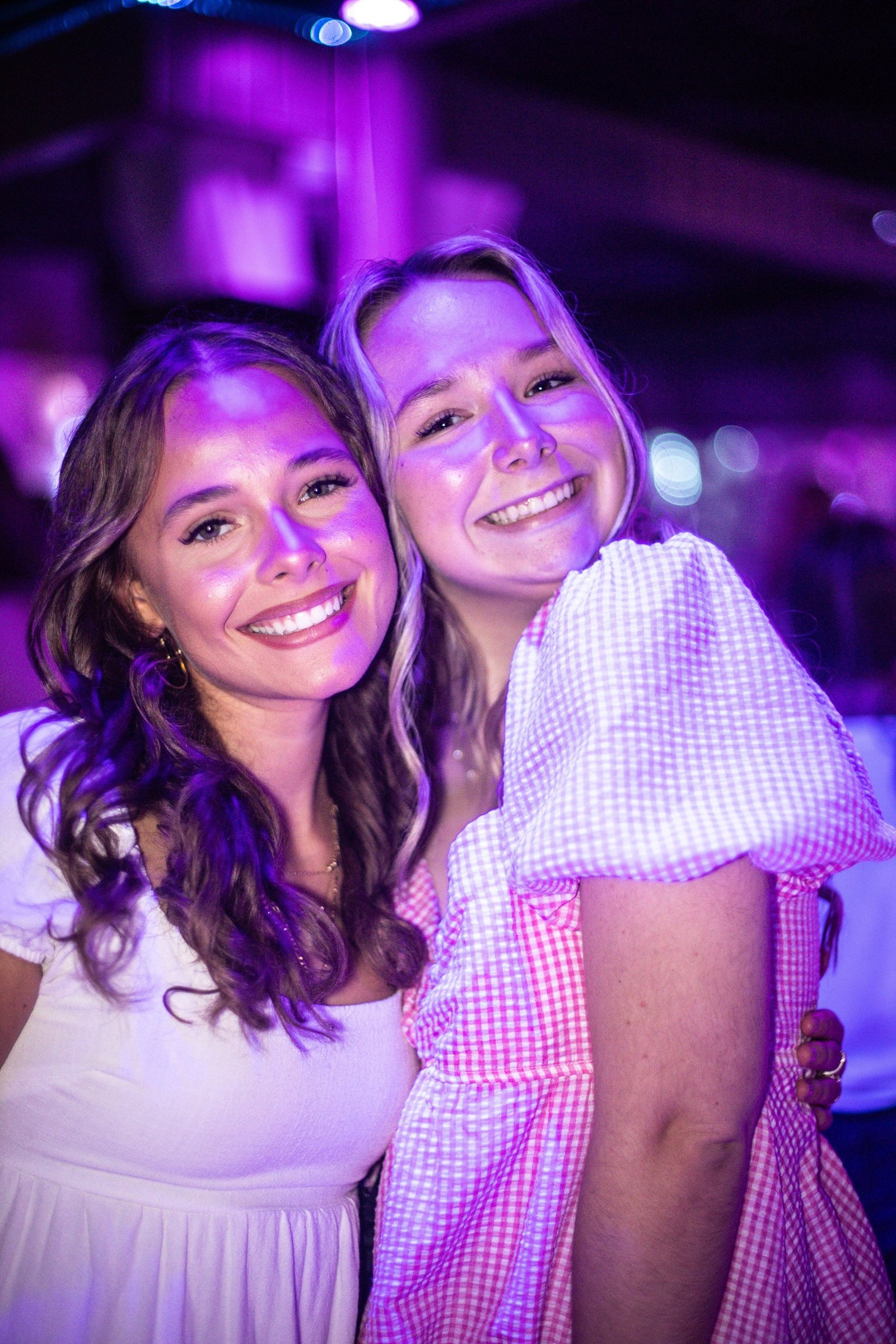 Two friends smile together under purple event lighting.