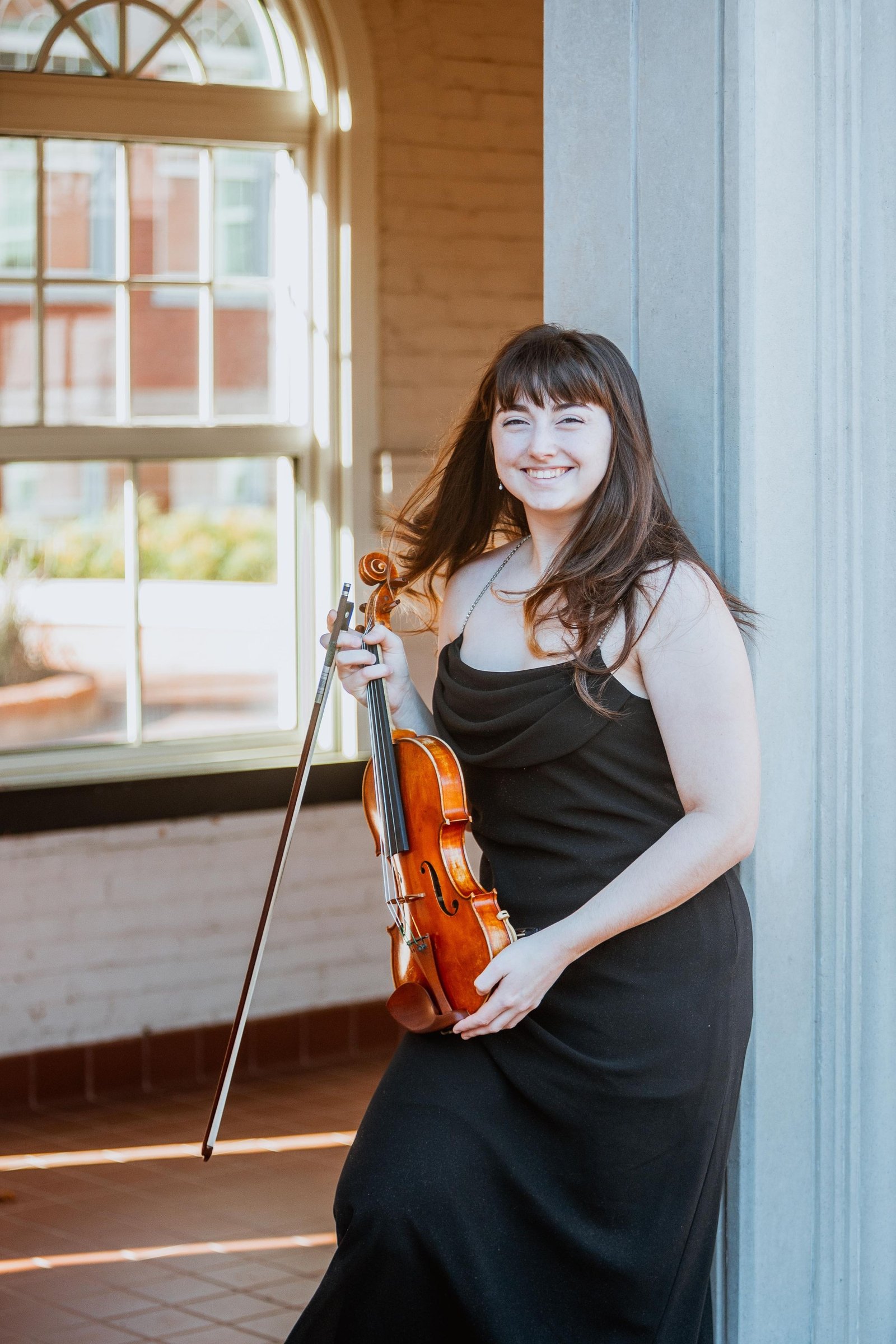 Portrait of a violinist holding her violin beside a window.