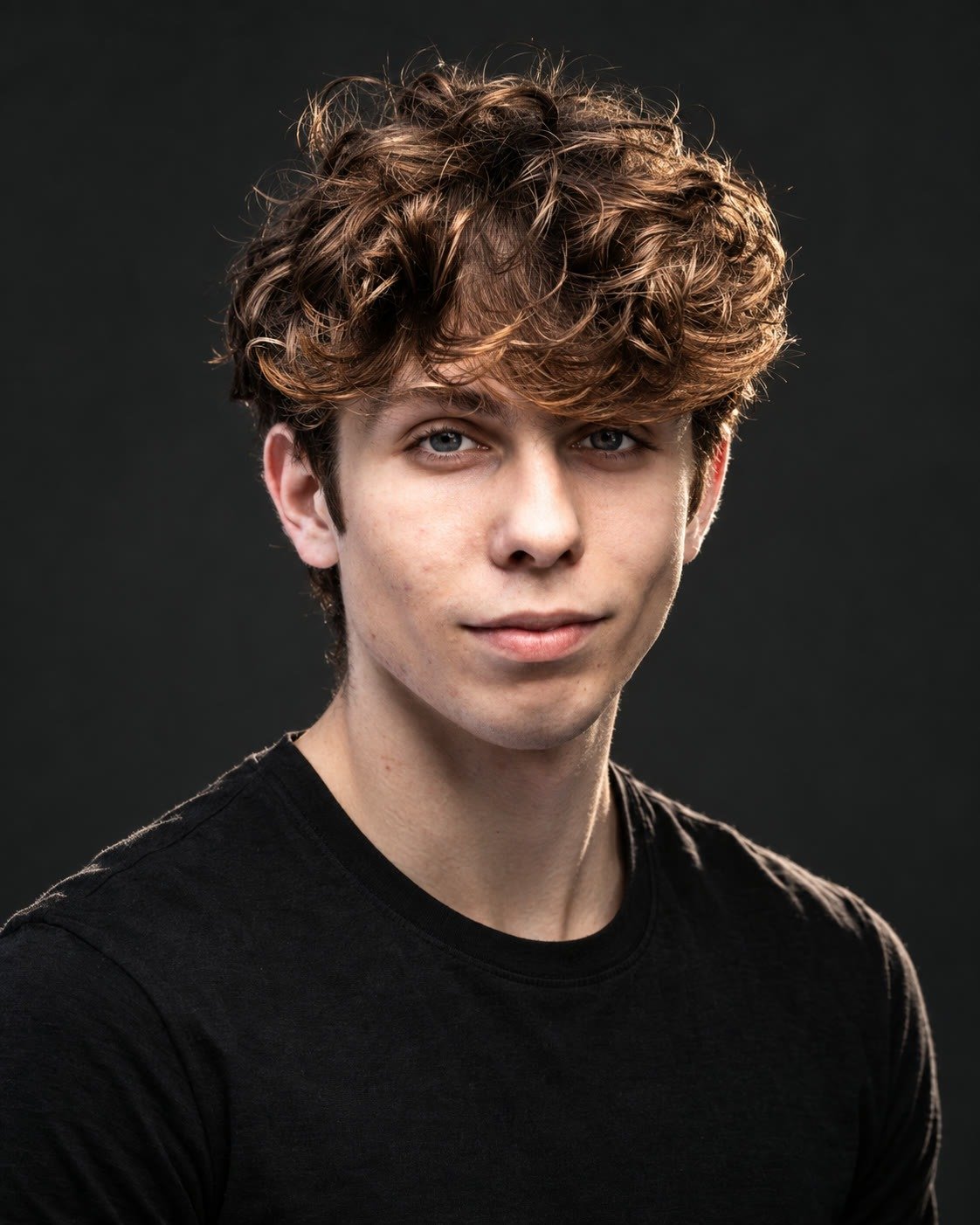 Portrait of Gabe Key, a young man with curly brown hair in a black shirt, lit from one side against a plain dark studio backdrop.